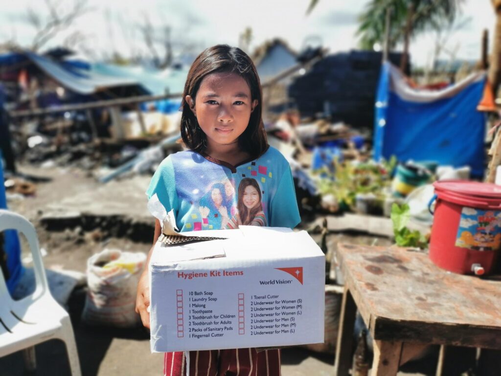Filippiiniläinen lapsi hygieniapakkauksen kanssa katastrofin keskellä.