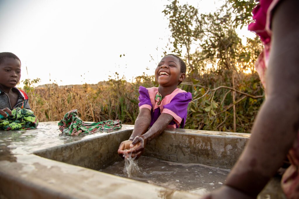 Malawilainen pikkutyttö pesemässä iloisesti kädet puuhtaan veden lähteellä.
