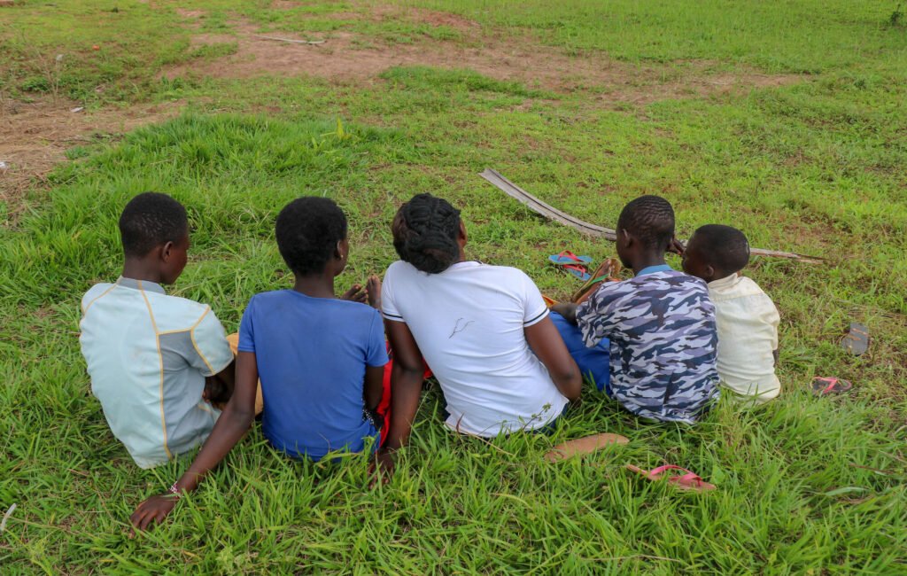 Entisiä lapsisotilaita Kongon demokraattisessa tasavallassa istuvat ruohossa, selät kameraa päin.