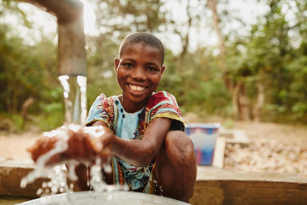 Ghanalainen tyttö pesee kädet uudella vesipisteellä ja hymyilee kameralle.