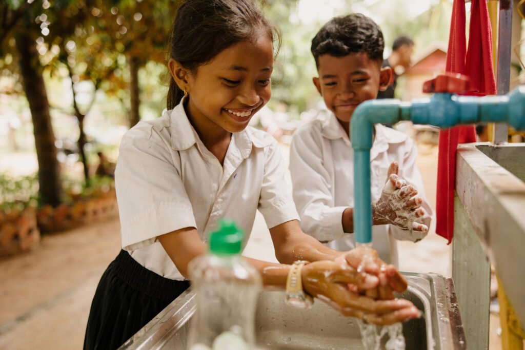 Kambodzalainen koulutyttö ja -poika pesevät hymyillen kädet pesupisteellä.