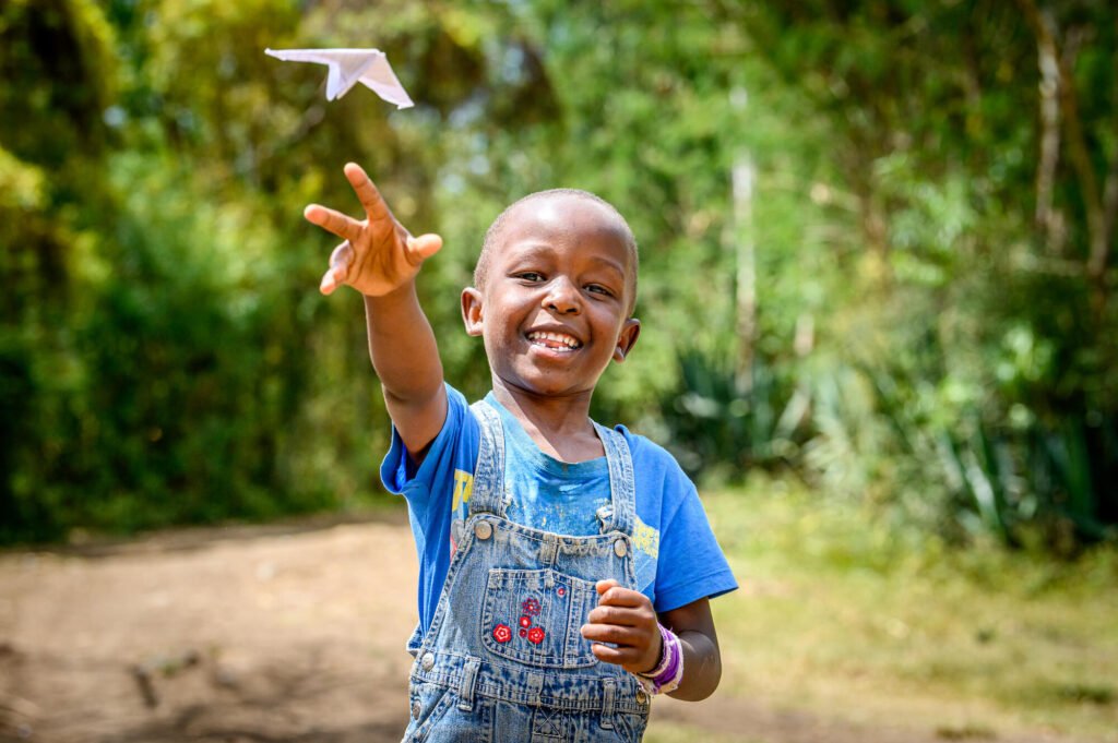 Kenialainen poika heittää paperilentokoneen kameraa päin, leveästi hymyillen.