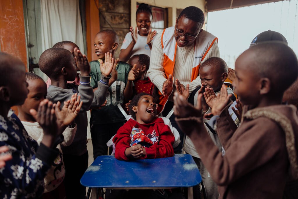 12-vuotias Sandra istuu uudessa, World Visionilta saamassa, pyörätuolissaan ja nauraa ympärillä olevien lasten ja World Vision -työntekijän kanssa.