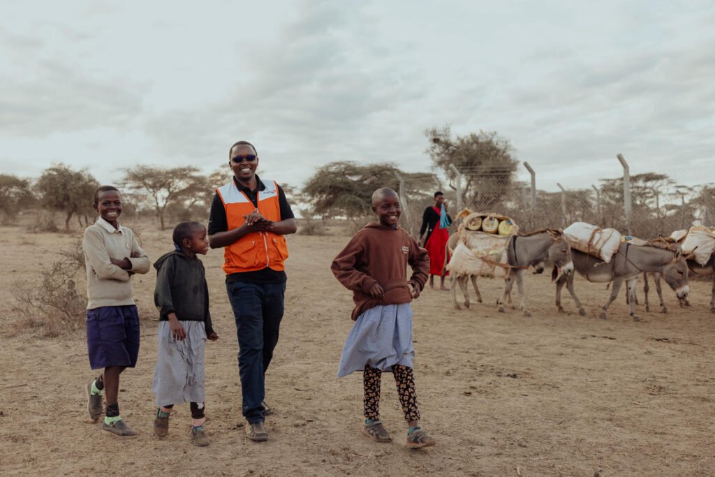 World Vision Kenian työntekijä kävelee juttelemassa hymyillen kolmen lapsen kanssa.