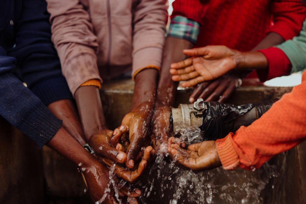 Lähikuva lasten käsistä leikkimässä puhtaalla vedellä vesipisteellä Keniassa.