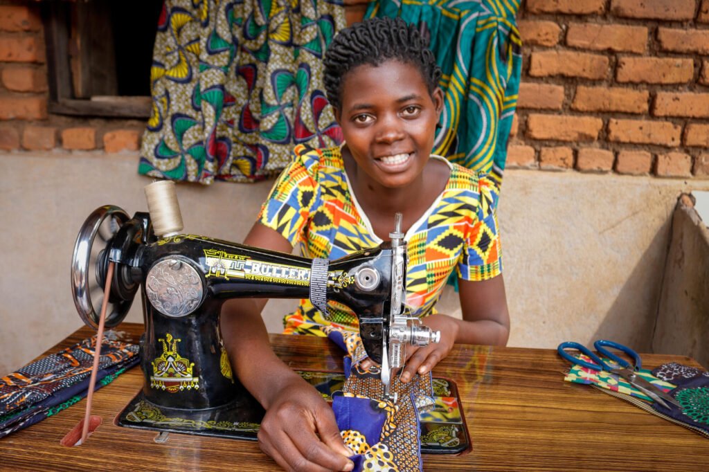 Malawilainen nuori nainen hymyilee kameralle ompelukoneellaan.