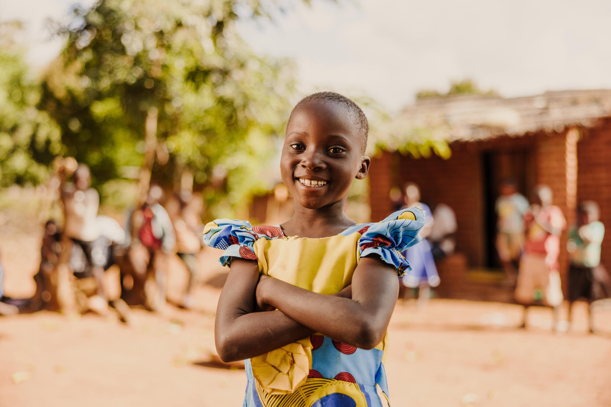 Malawilainen tyttö seisoo kädet puuskassa ja hymyilee itsevarmasti kameralle.