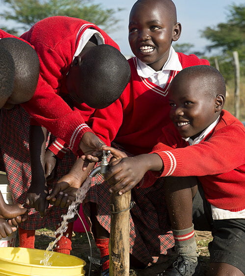Meibekiläiset lapset käyttävät nauraen uutta puhtaan veden vesipistettä.