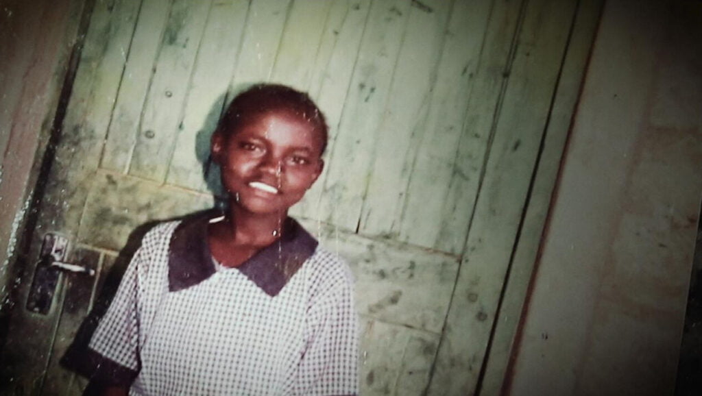 Valokuva nuoresta Nancystä koulupuku päällä hymyilee kameraan.