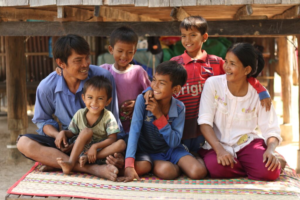 Kambodzalaiset vanhemmat istuvat neljän poikansa kanssa lattialla. Kaikki nauravat yhdessä.