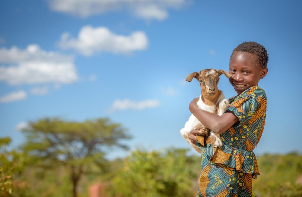 Sambialainen tyttö pitää vuohta sylissään ja hymyilee kameralle.