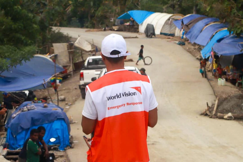 World Visionin paikallinen työntekijä Timor Lestessä katsoo tietä, jonka varrella on sinisiä ja valkoisia telttoja.