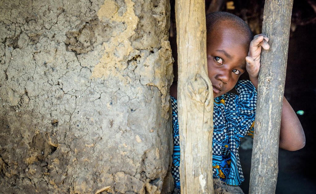 Ugandalainen tyttö kurkkaa kameraa talon sisältä.