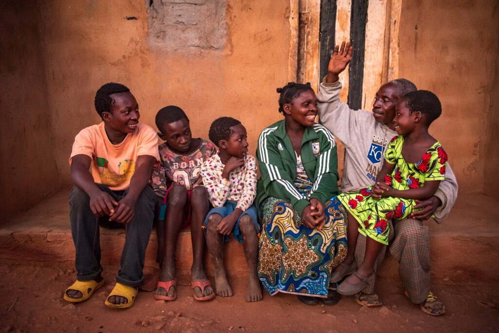 Sambialainen perhe istuu yhdessä penkillä ja nauravat. Pienin tyttö istuu isänsä sylissä.