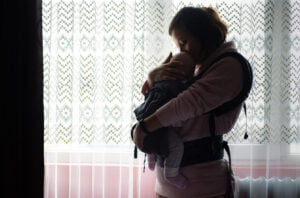 Ukrainalainen äiti seisoo ikkunan edessä ja pitää vauvansa sylissään.