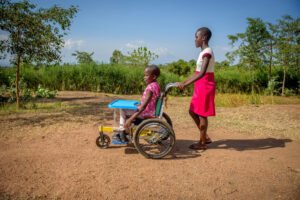 Kenialainen tyttö työntämässä pikkusiskoaan pyörätuolissa.