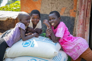 Kolme lasta nojaavat World Visionilta saaneita ruokasäkkejä vastaan.