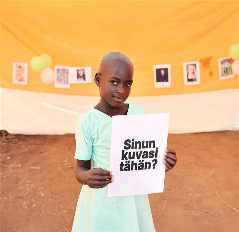 Ugandalainen tyttö katsoo kameraan ja pitää kuvaa kädessään