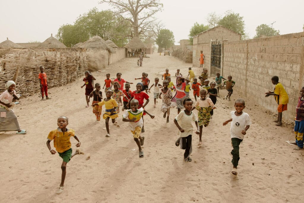 Senegalilaisia lapsia juoksemassa iloisesti kotikylässään.