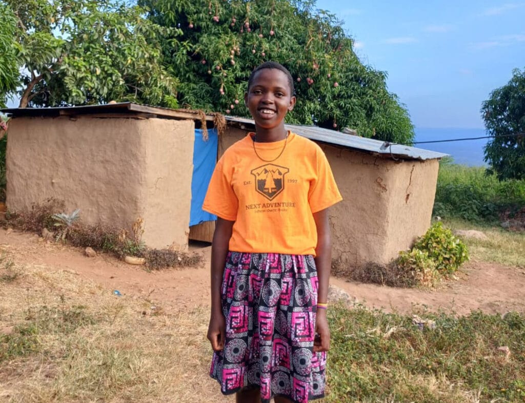 Chatiry seisoo hymyillen oman kotinsa edessä Ngoswetissa. Koti on hyvin pieni savimaja.