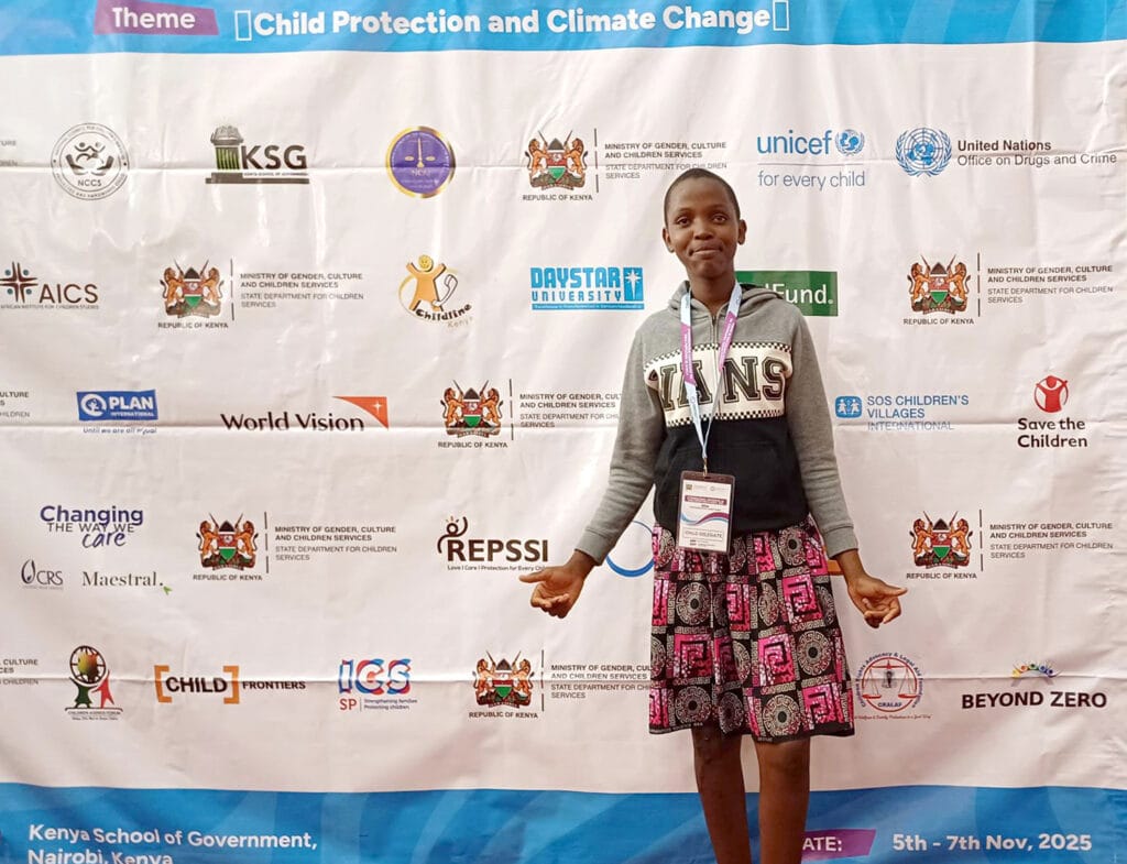 Charity poseeraa Ngoswetin konferenssissa logoseinän edessä.