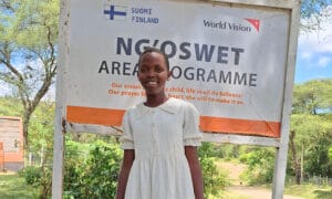 Charity Ngoswetin kummiohjelman kyltin edessä.