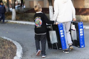 Ukrainalainen poika auttaa äitiään kantamaan kahta lämpöpatteripakkausta.