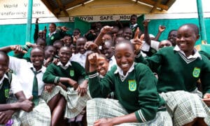 Kymmeniä tyttöjä istumassa hymyillen turvatalon edessä Kenian Alalessa.