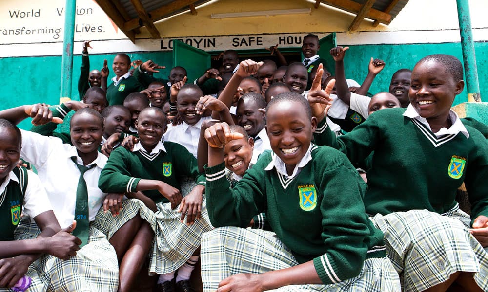 Kymmeniä tyttöjä istumassa hymyillen turvatalon edessä Kenian Alalessa.