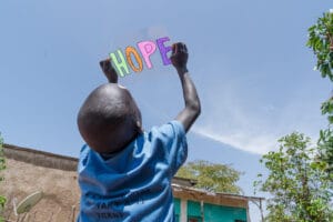 Etiopialainen kummilapsi pitää muovikalvoa käsissään kohti taivasta. Muovikalvossa lukee värikkäillä kirjaimilla sana "Hope", eli toivo.