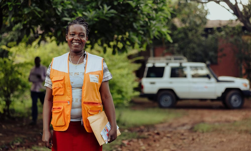 Etiopialainen World Vision työntekijä hymyilee kameralle. Taustalla näkyy World Visionin auto.
