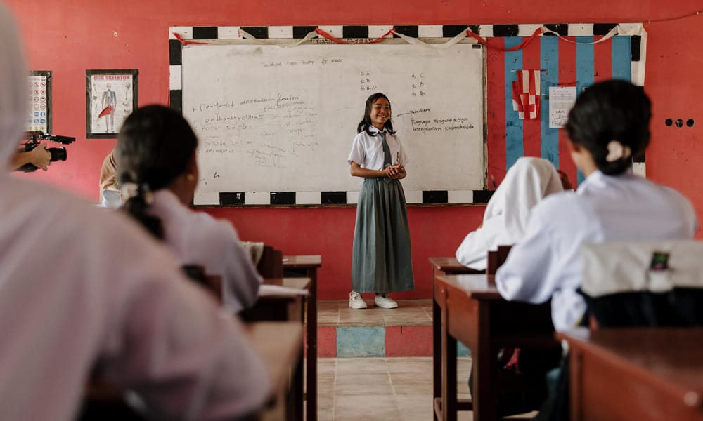 Indonesialainen tyttö seisoo luokansa edessä taululla.