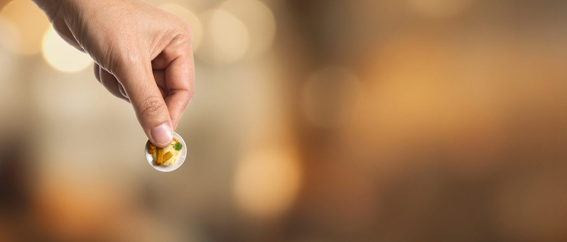Käsi pitää sormien välissä kiinni kahden euron kolikon, mutta kun katsoo tarkemmin, kolikko osoittautuu lautaseksi, jossa on perunamuussia sekä kalapuikkoja numero 2-muodossa.