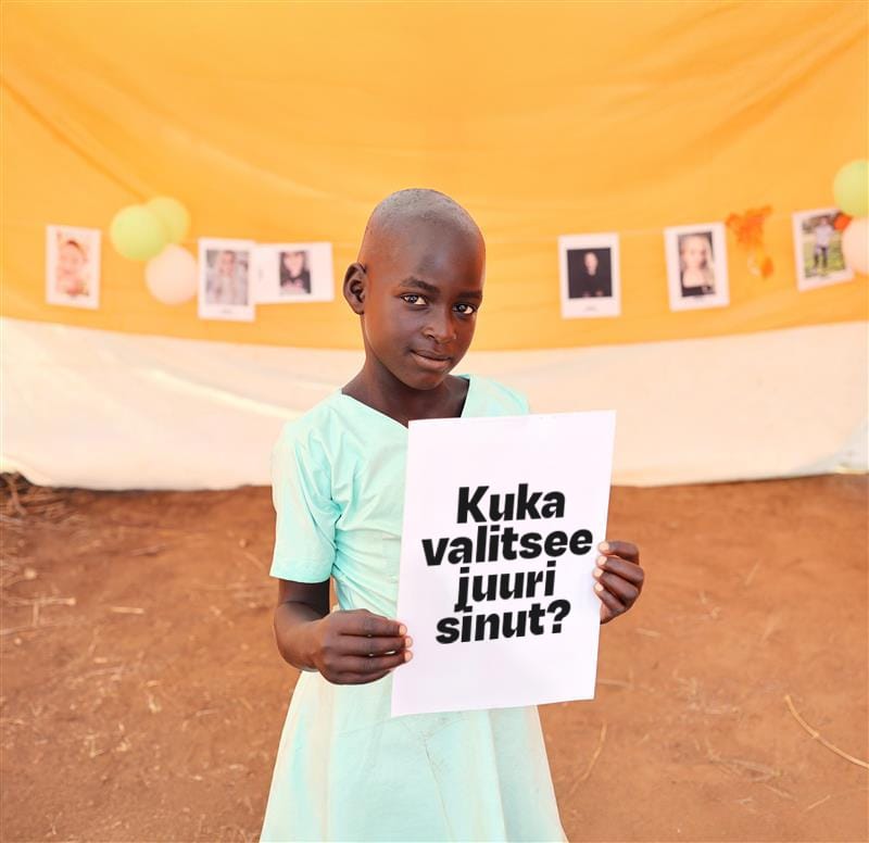 Ugandalainen tyttö katsoo kameraan ja pitää kuvaa kädessään